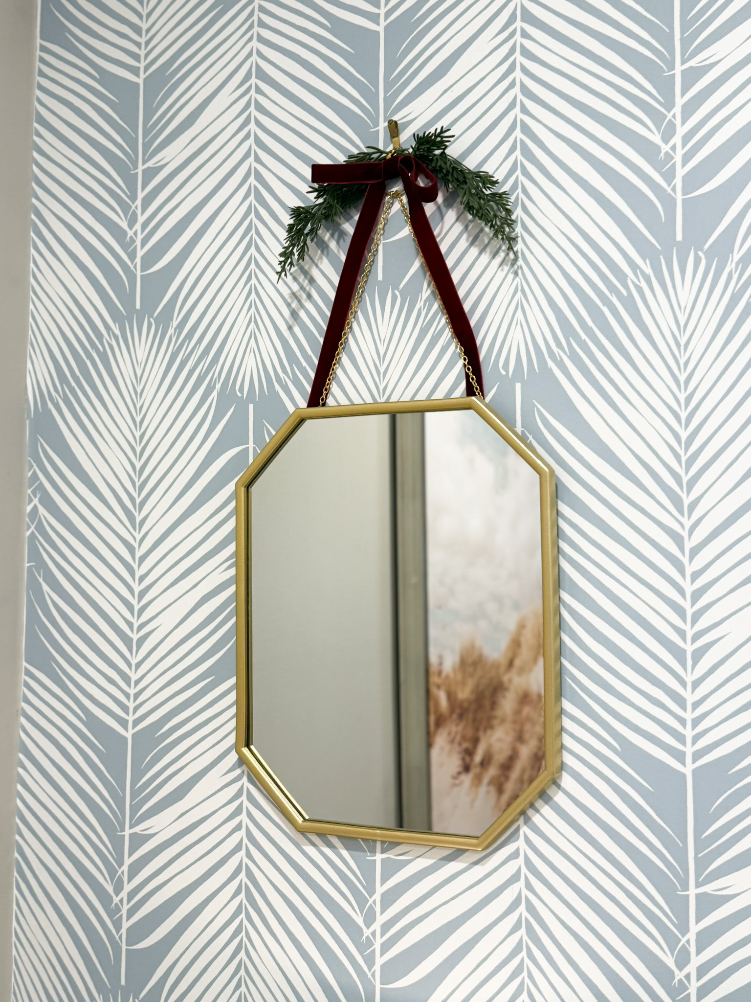 Delicate gold mirror with evergreen accent and ribbon